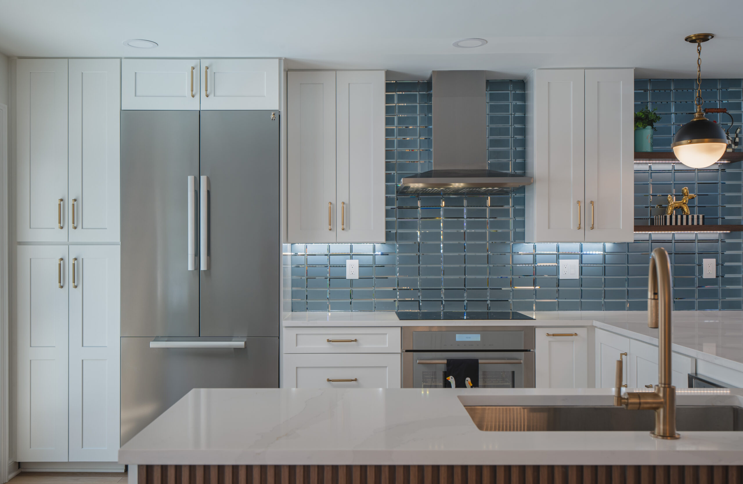 Straight-on shot of a glossy teal glass subway tile backsplash with a stainless steel range hood and white shaker cabinets.