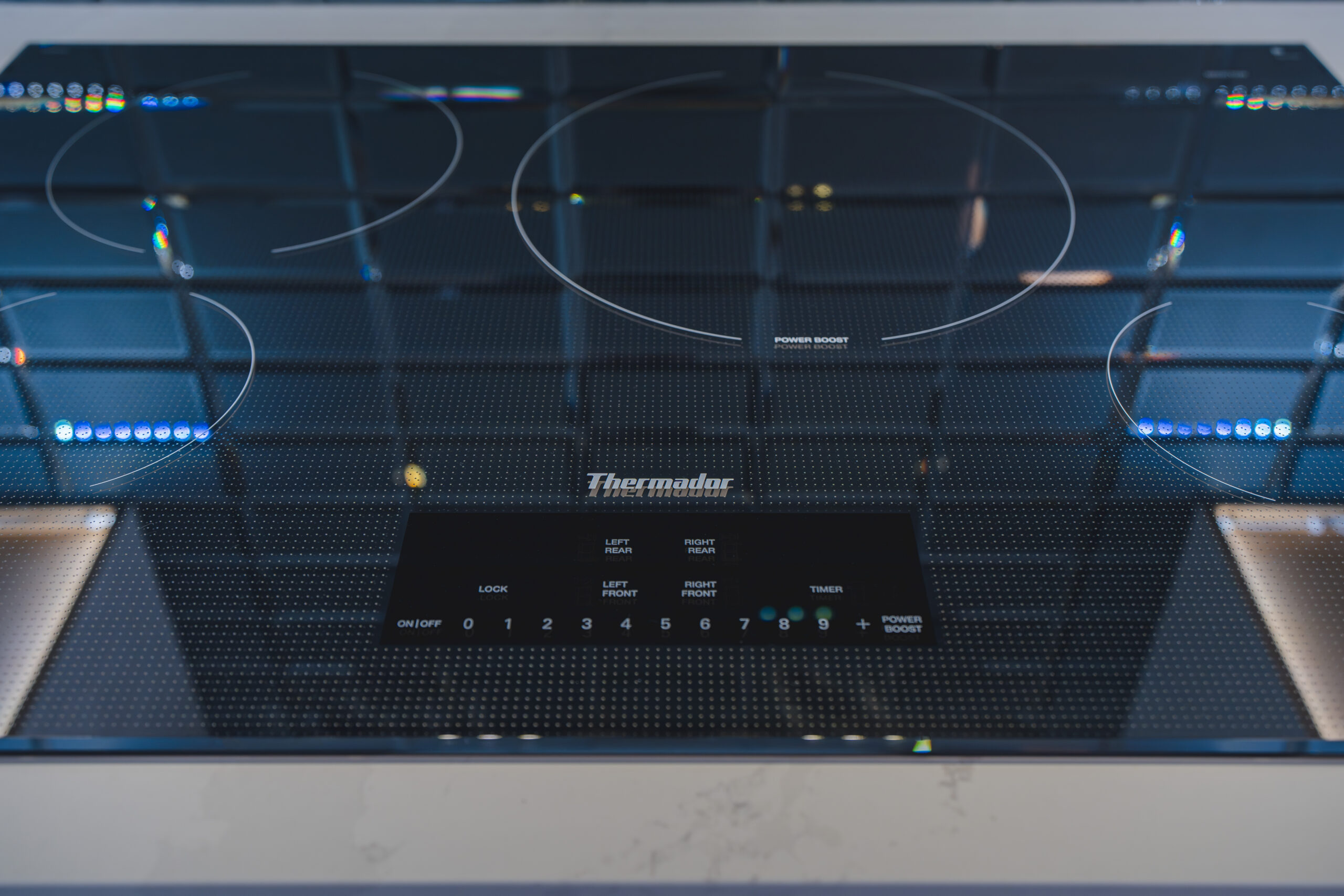 Close-up of a black glass Thermador induction cooktop integrated into a white quartz countertop.
