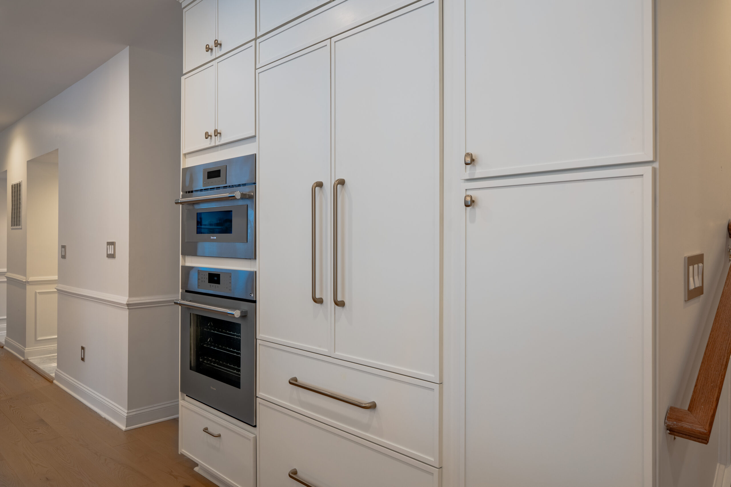 A detailed shot of stainless steel Thermador ovens built into minimalist white cabinetry with sleek gold handles.