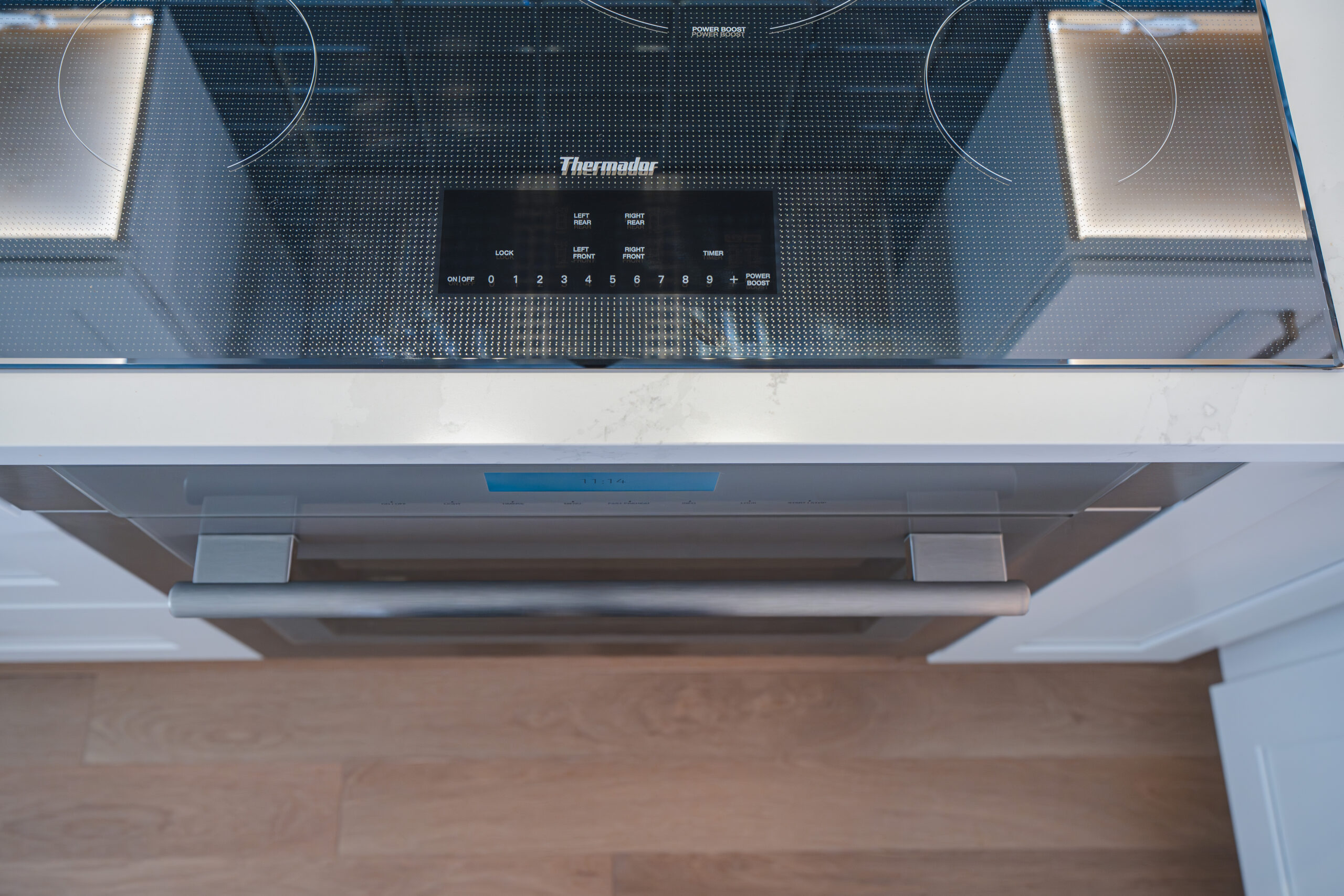 Top-down view of a Thermador induction cooktop and the stainless steel handle of a built-in oven.