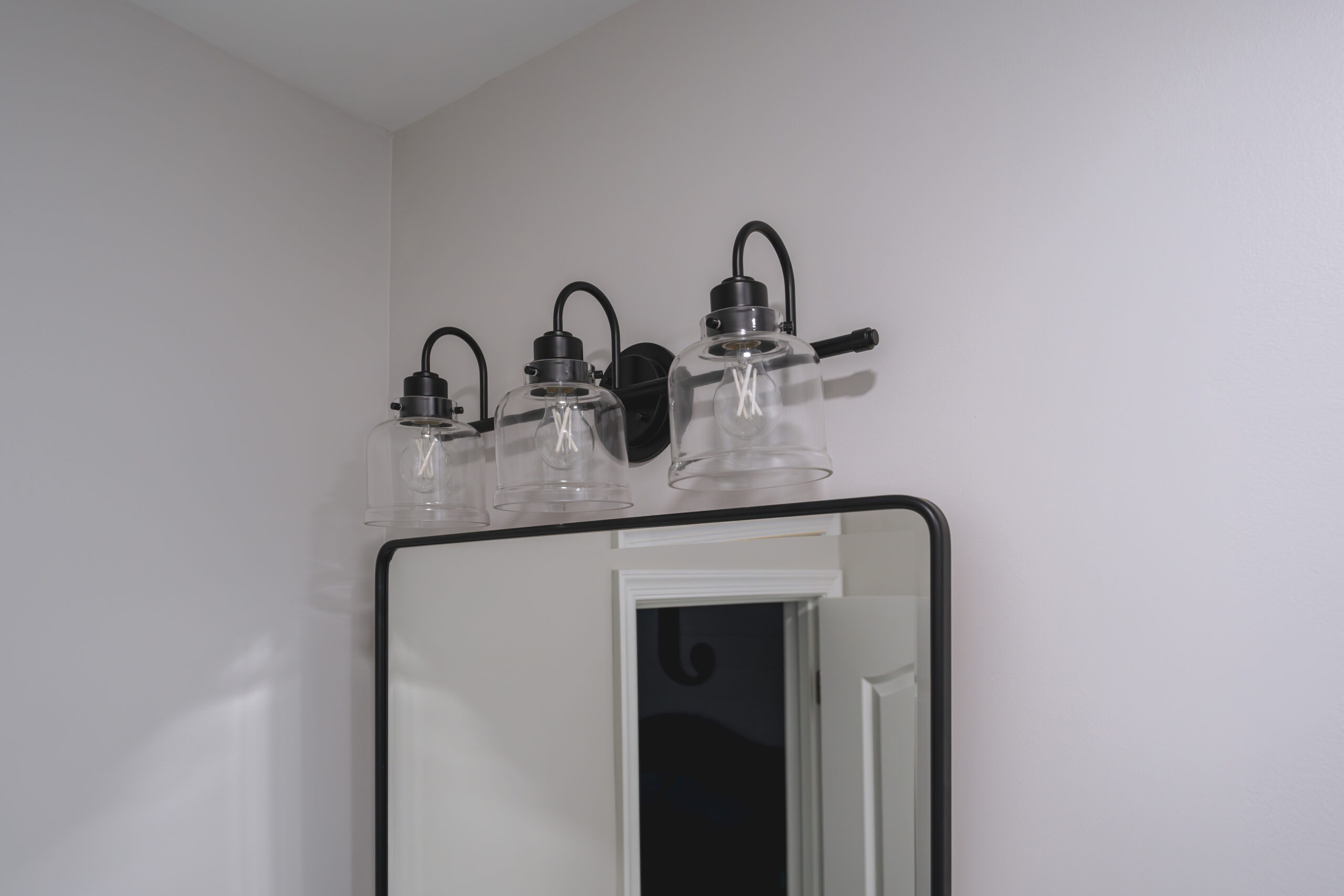 A black three-light vanity fixture with clear glass globes installed above a bathroom mirror.