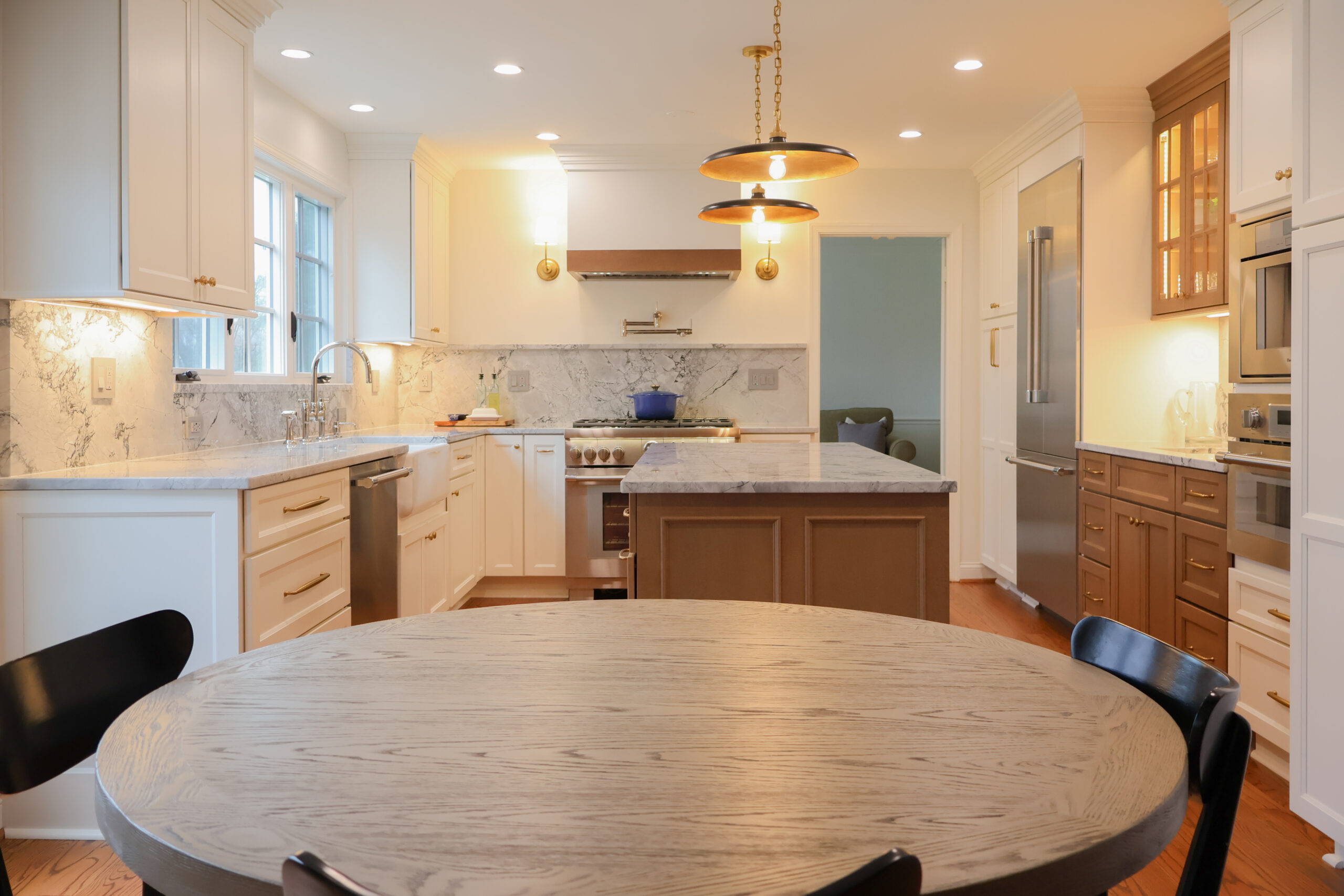 Open concept kitchen in Georgetown Washington DC with white shaker cabinets, a dark wood island, and designer brass pendant lights.
