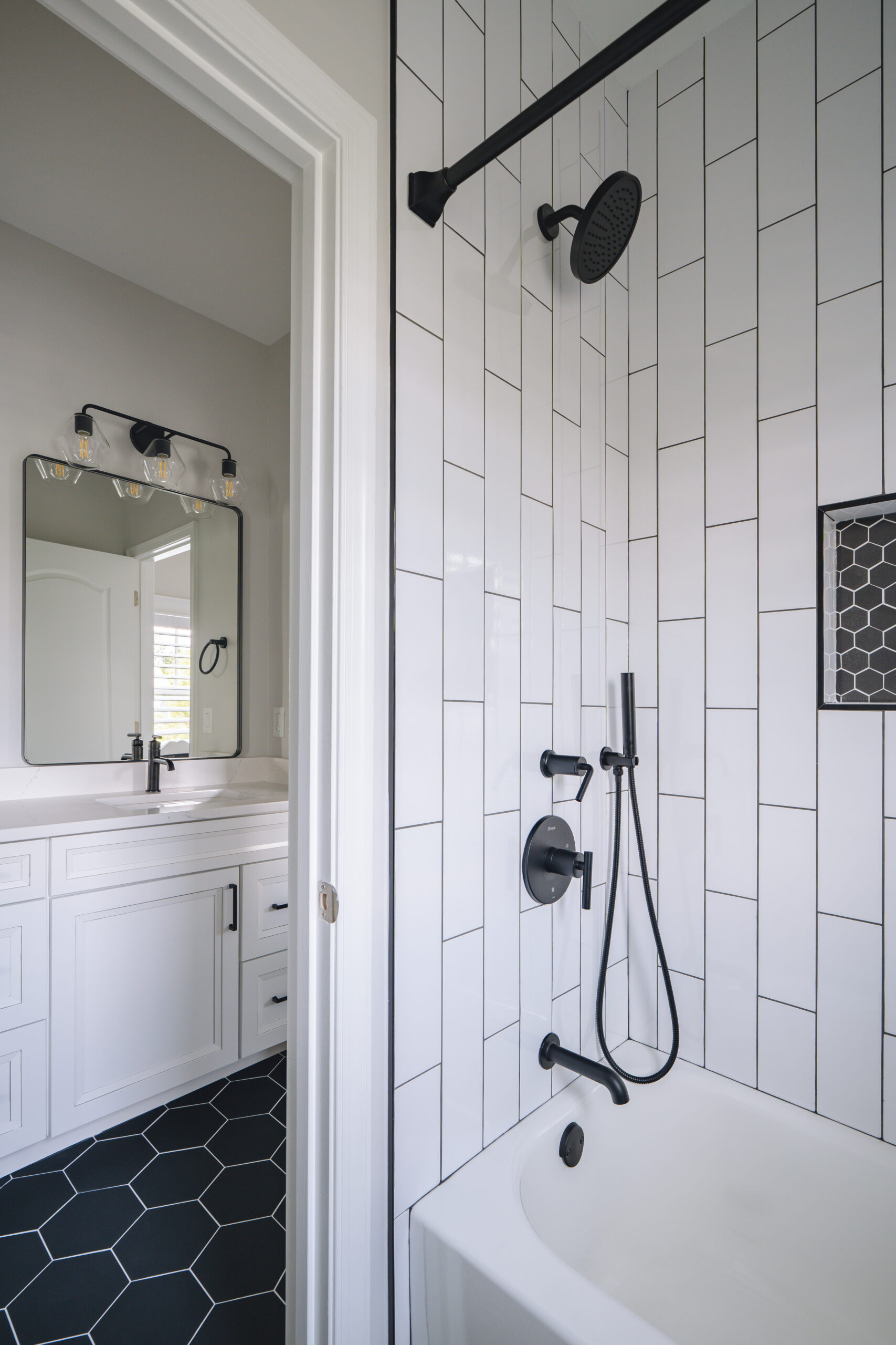 Detailed view of a white tub and shower area featuring matte black fixtures and vertical white subway wall tiles.