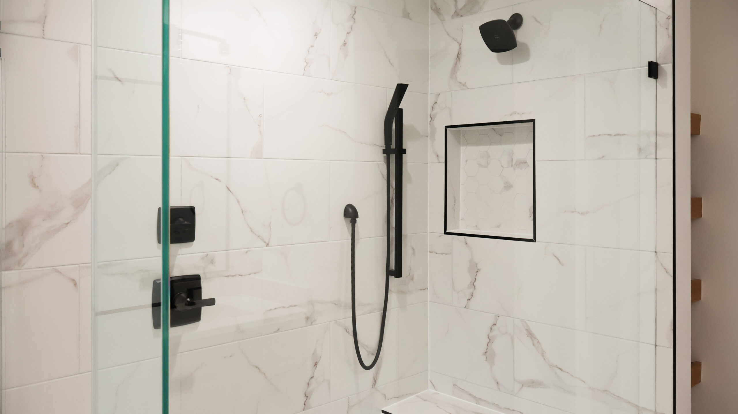 Detail of a walk in shower featuring large marble look wall tiles, a matte black showerhead, and a recessed shower niche.