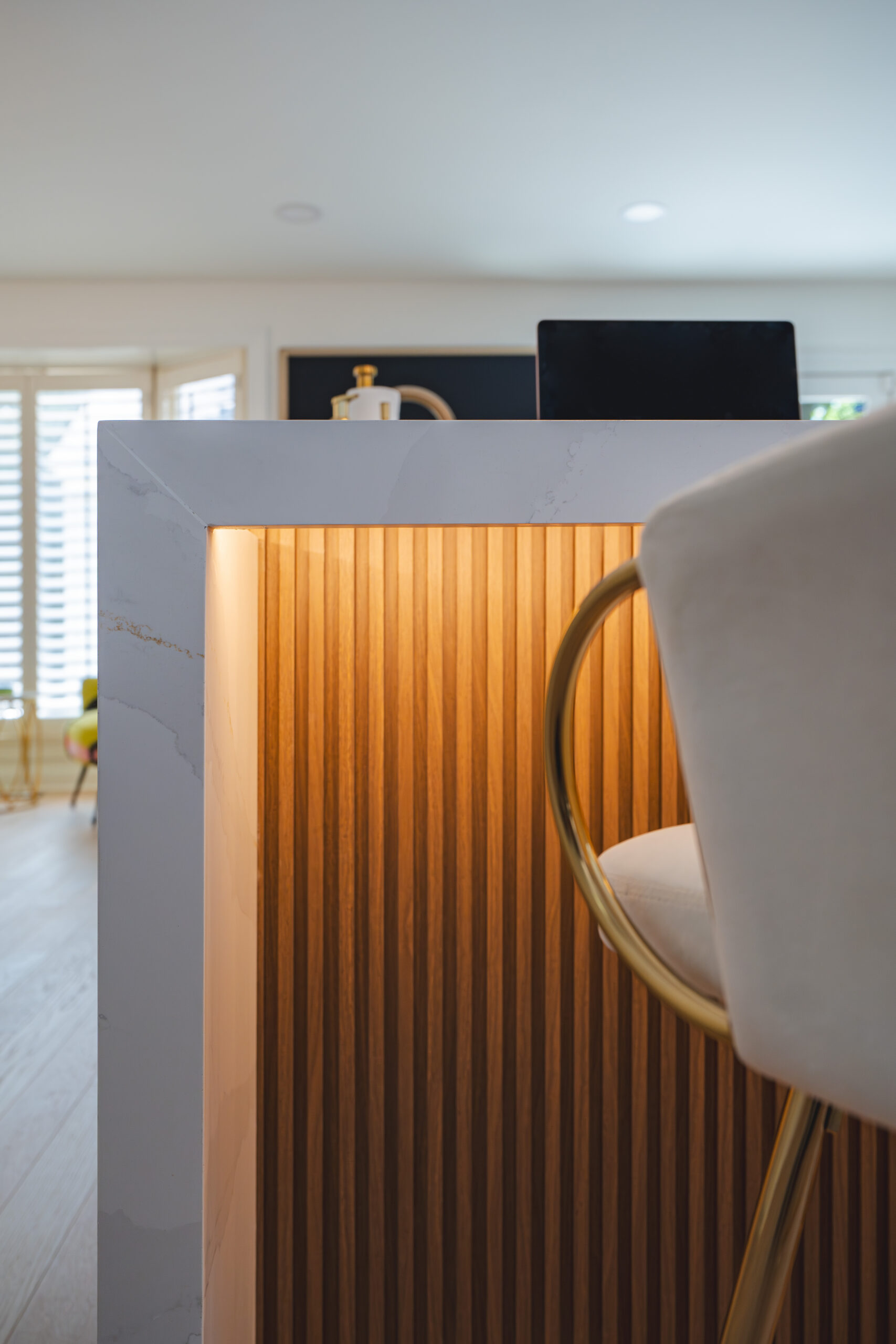 Vertical close-up of a white quartz waterfall edge and illuminated wood slats on a kitchen island.