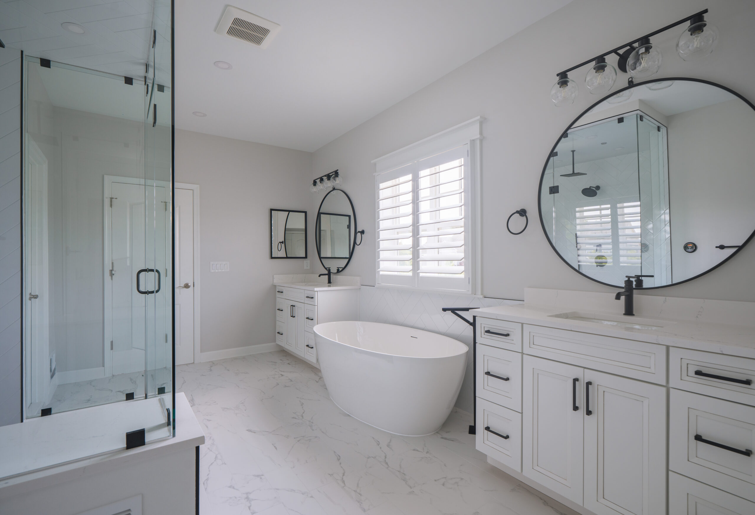 A white double bathroom vanity with marble countertops and round black-framed mirrors.