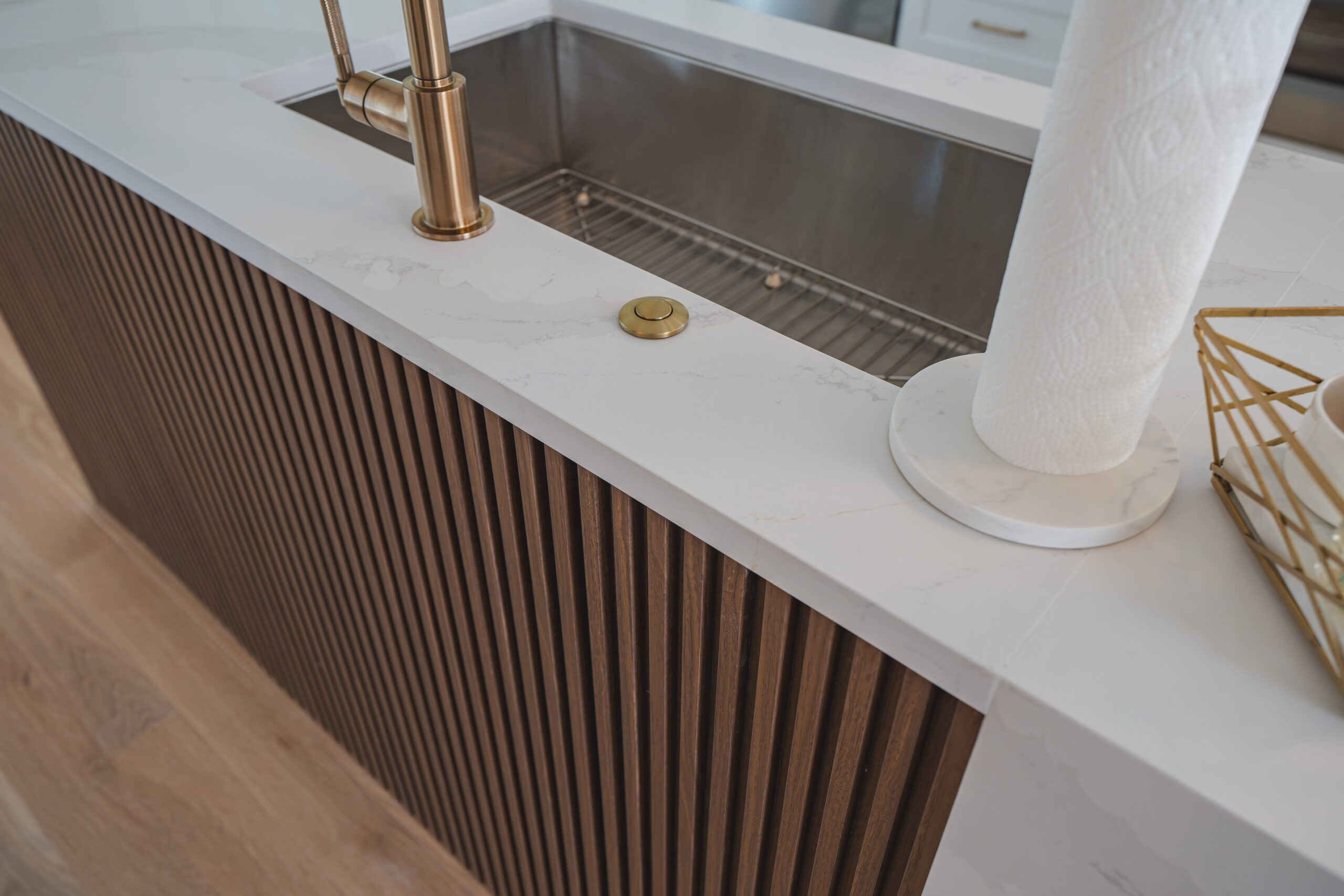A close-up of a gold air switch for a garbage disposal on a waterfall quartz countertop edge with fluted wood siding.