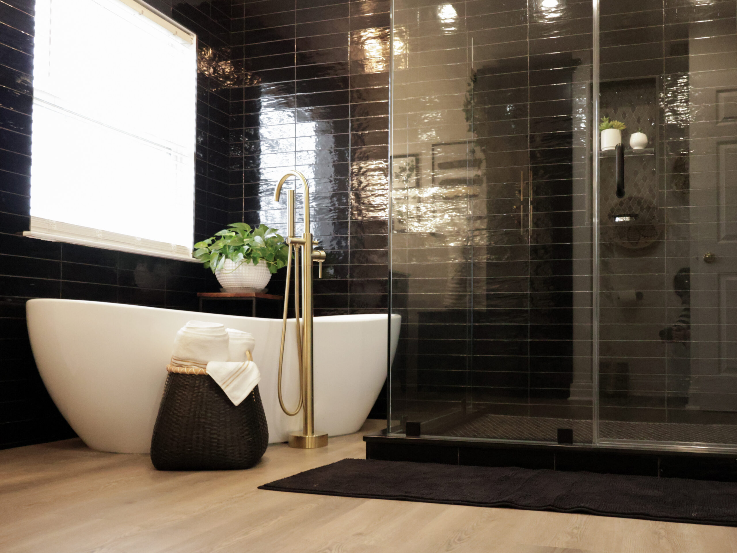 Luxury bathroom remodeling in Washington DC with glossy black wall tile, a white freestanding soaking tub, brushed gold floor-mount faucet, and frameless glass shower enclosure
