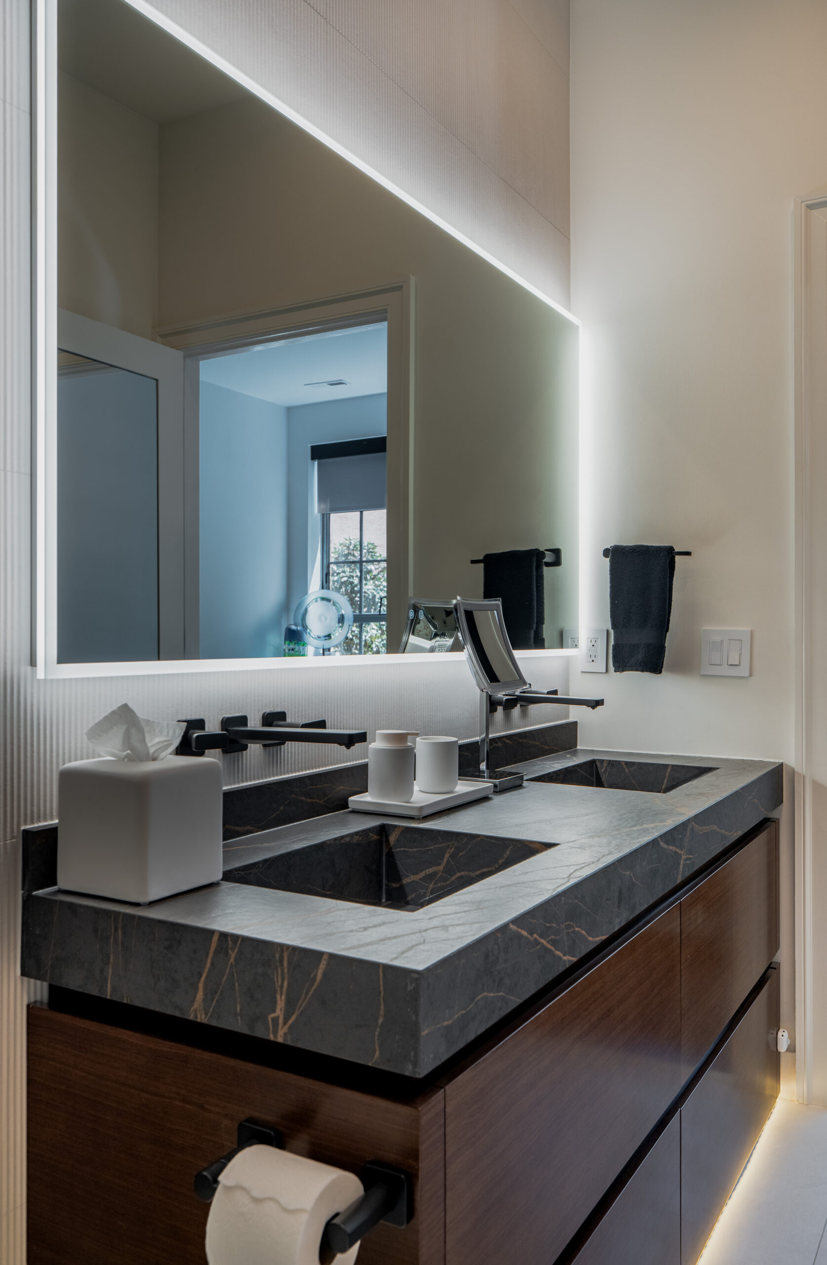 Black marble undermount sink vanity with gold veining, floating walnut cabinet with LED toe kick lighting, large backlit LED mirror, matte black wall-mounted faucet, and ribbed white tile backsplash in Washington DC bathroom remodel