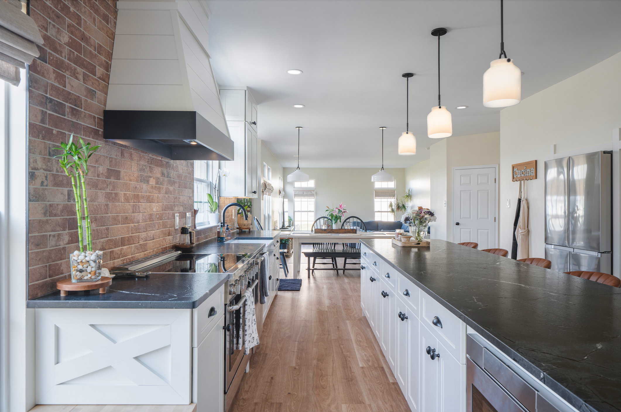 A farmhouse-style kitchen remodel in Cherry Hill, NJ with white cabinetry, an exposed brick backsplash, honed black countertops, a shiplap range hood, and an open-concept layout flowing into the living area.