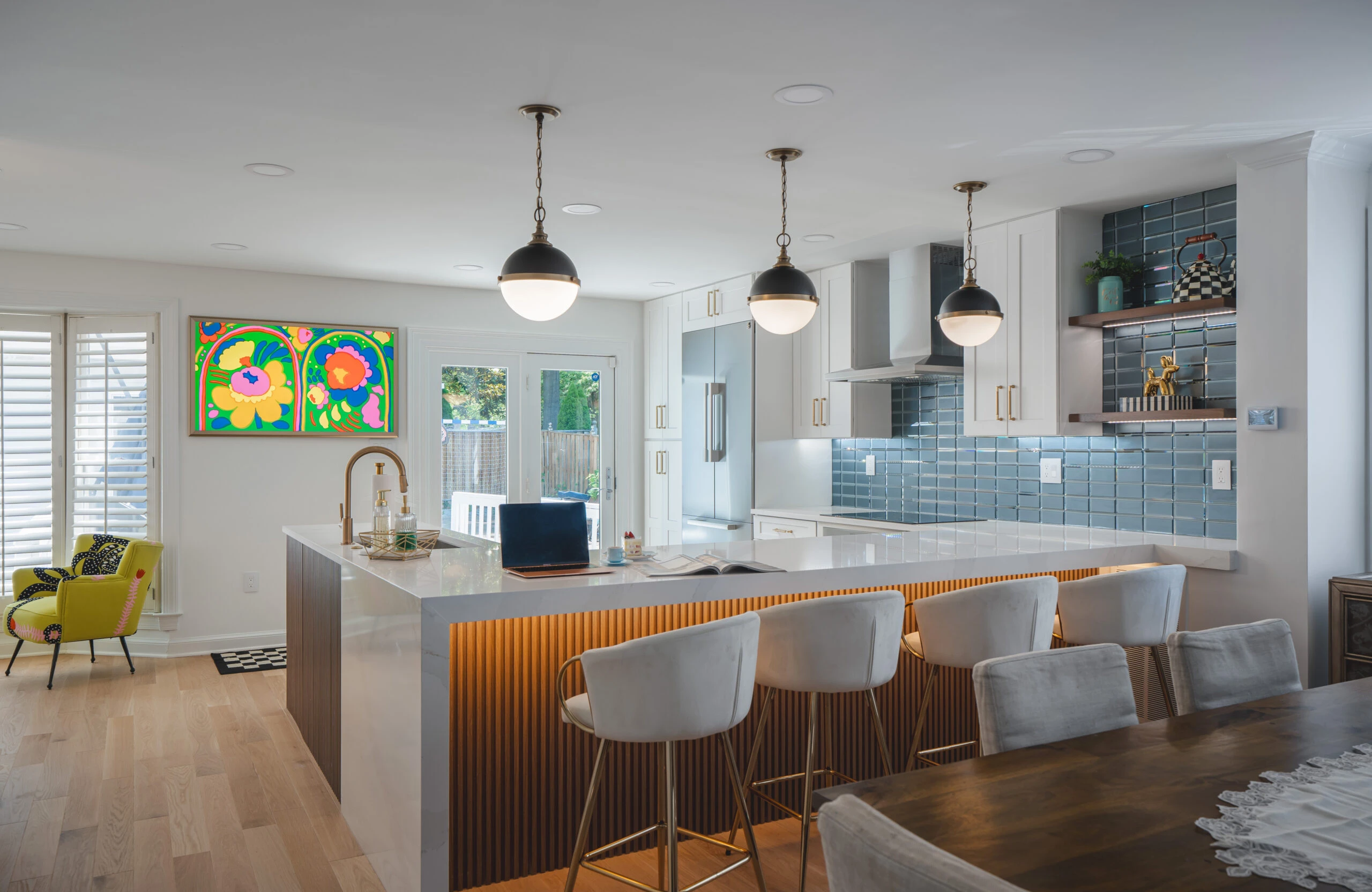 Home remodeling project in Fredericksburg, VA featuring a large custom kitchen island with quartz countertop, full-height blue subway tile backsplash, white shaker cabinets, brass pendant lights, and hardwood flooring by Build Design Center