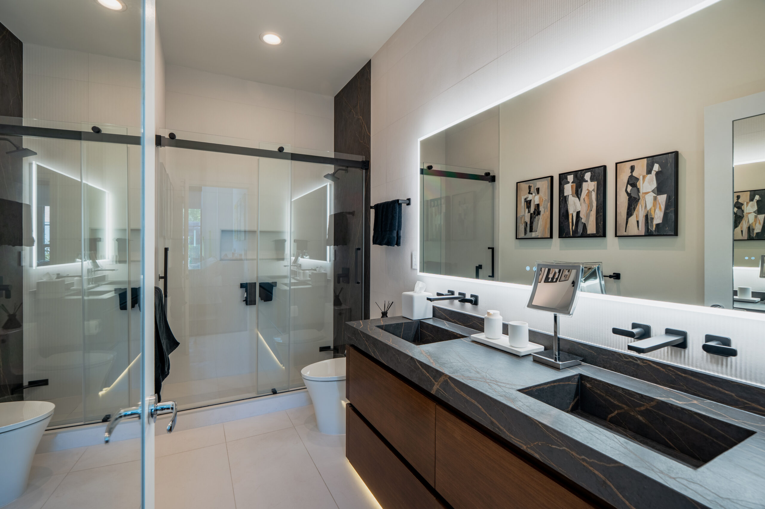 Luxury master bathroom remodel featuring black marble double vanity with undermount sinks, matte black wall-mounted faucets, large backlit LED mirror, frameless sliding glass shower door, and dark marble accent wall in Washington DC