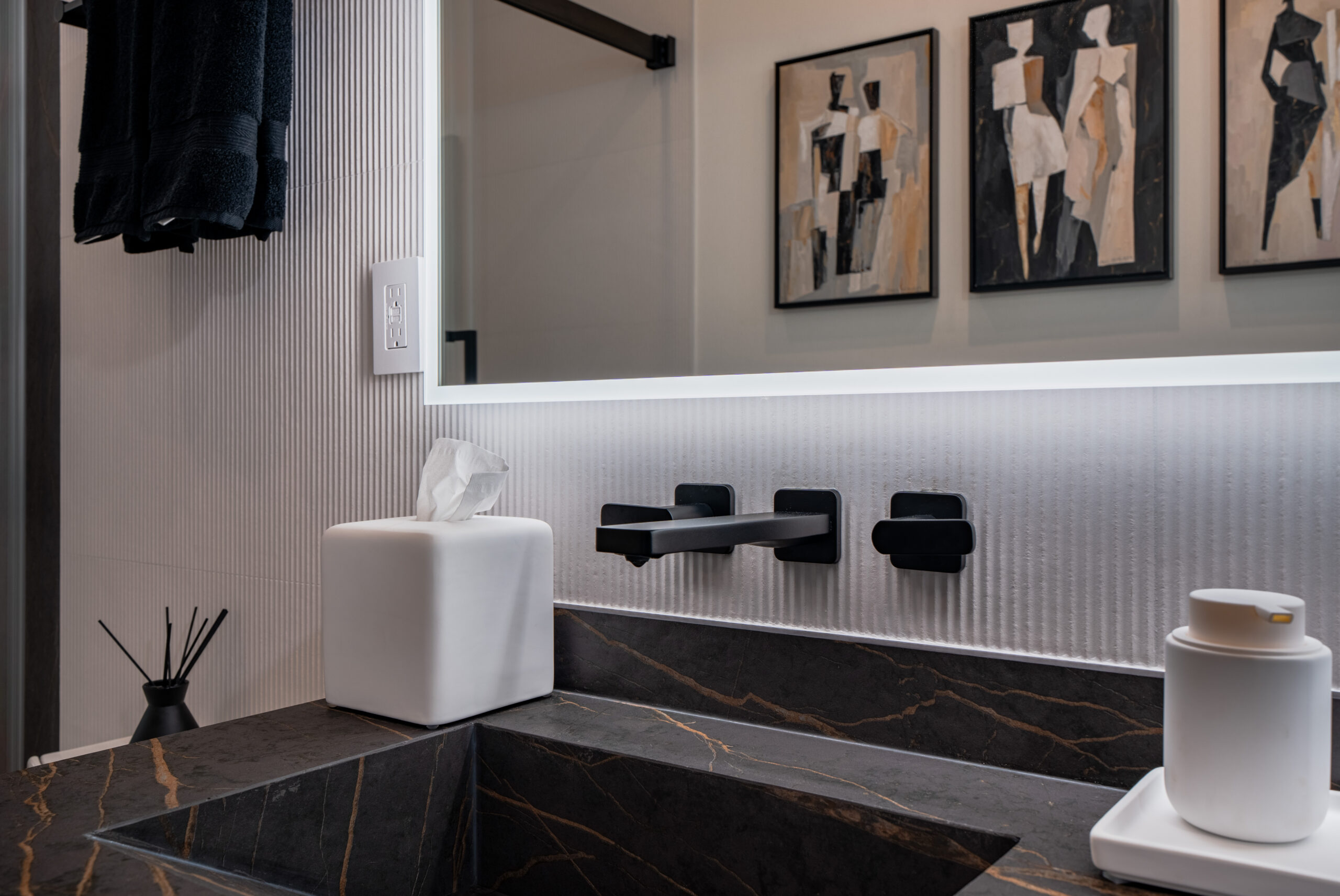 Close-up detail of matte black wall-mounted faucet and controls set into ribbed white tile backsplash above black marble undermount sink with gold veining in Washington DC luxury bathroom remodel