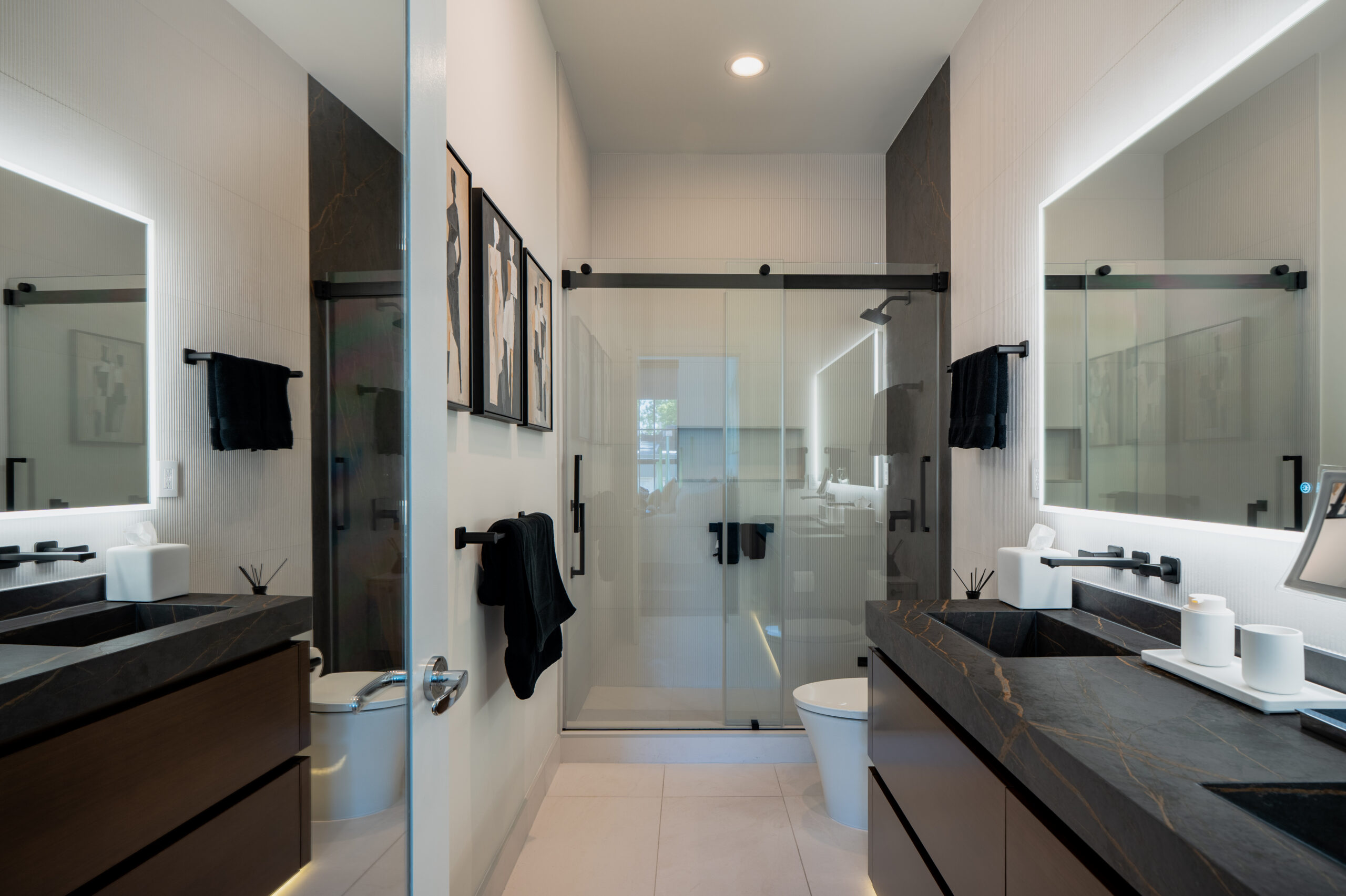 Symmetric wide-angle view of modern master bathroom remodel with dual black marble vanities, backlit LED mirrors, frameless sliding glass shower enclosure, ribbed white wall tile, and matte black fixtures in Washington DC
