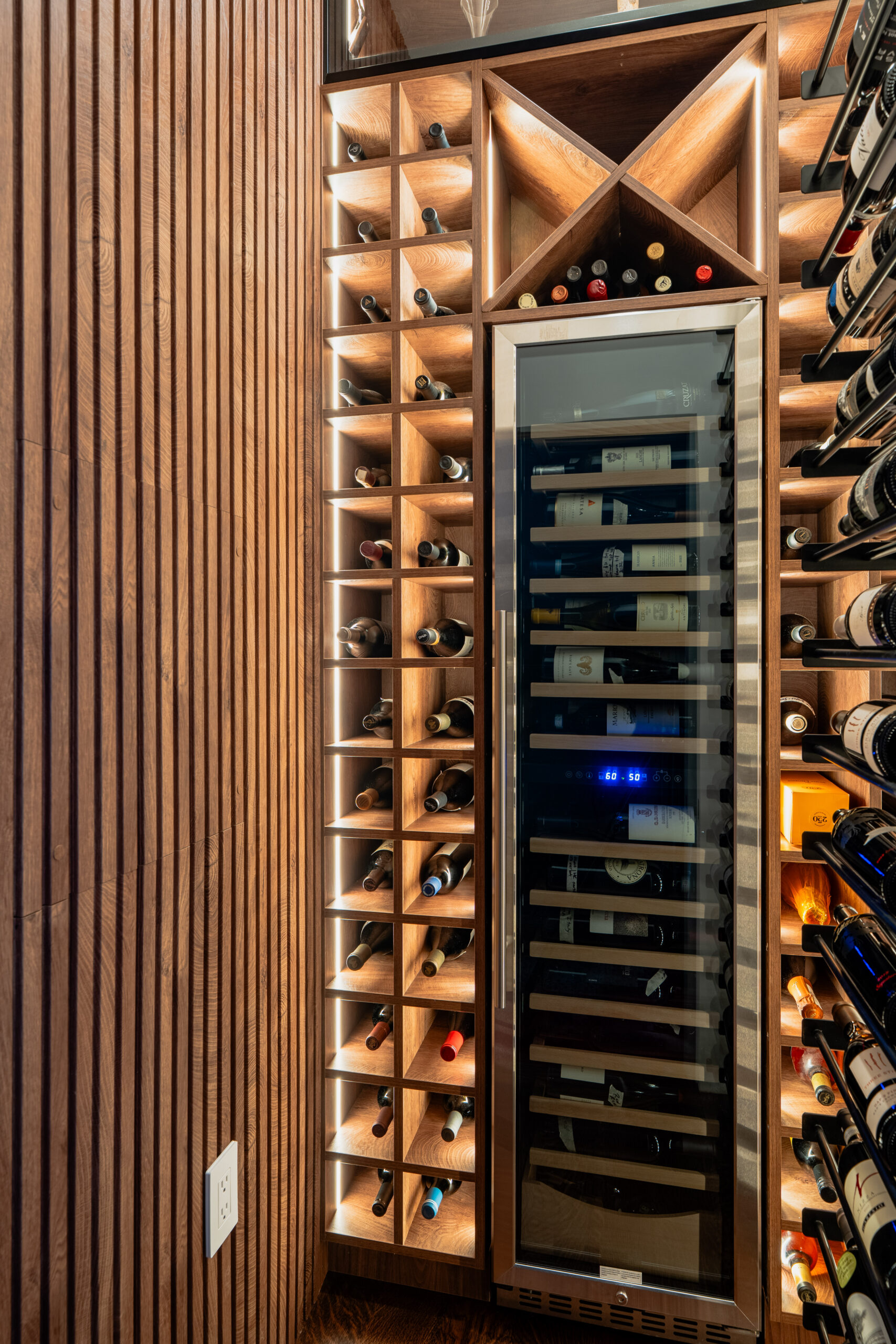 Walk-in wine cellar with backlit walnut grid wine racks, vertical slatted wood accent wall, and stainless steel dual-zone wine cooler in Washington DC luxury home renovation