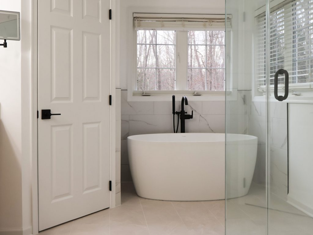 Bathroom remodel in Bethesda Maryland with a freestanding soaking tub, frameless glass shower enclosure, marble wall tile, and custom wood vanity with black fixtures