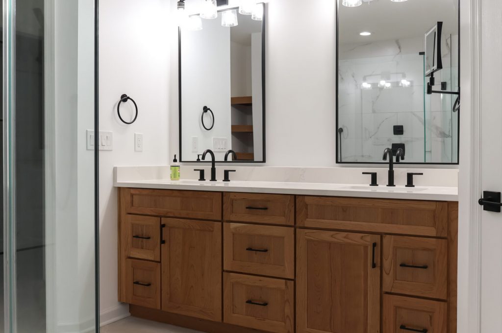 A warm and inviting modern bathroom featuring a red brick accent wall, white cabinetry with a marble countertop, and light wood laminate flooring that ties the rustic and contemporary elements together.